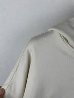 Cream hoodie side panel with stitched seam and slight fraying near shoulder