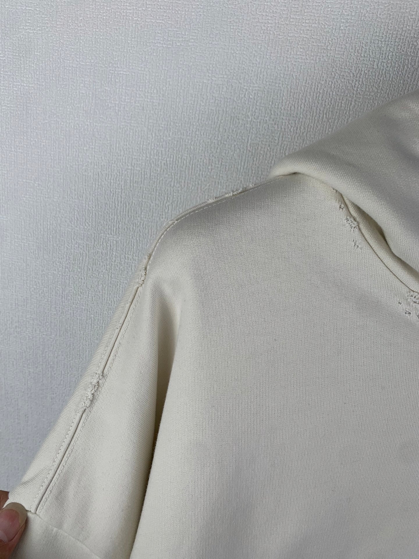Cream hoodie side panel with stitched seam and slight fraying near shoulder