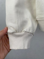 Cream hoodie cuff and hem with ribbed trim and frayed edge; hand holding