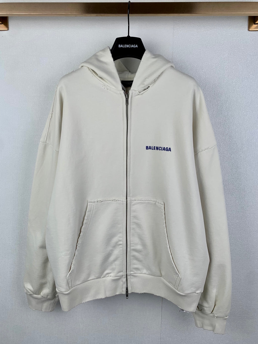 Cream zip-up hoodie with hood, front pockets, and blue BALENCIAGA chest logo