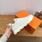White lace-up sneakers with thick cushioned sole, shown with hand, Hermes style