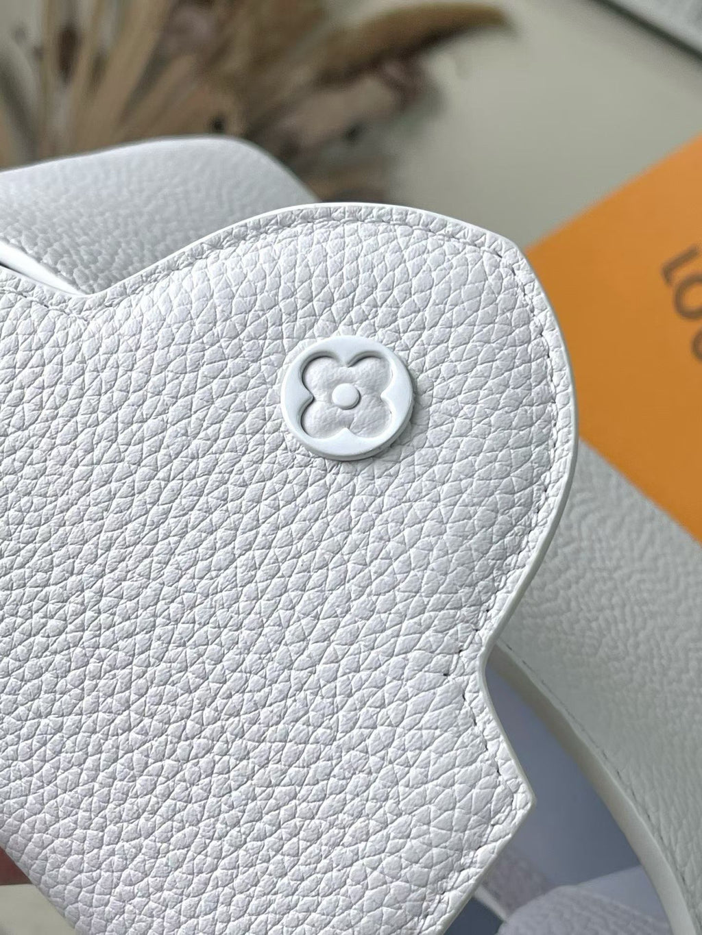 Louis Vuitton clover emblem on white textured leather flap
