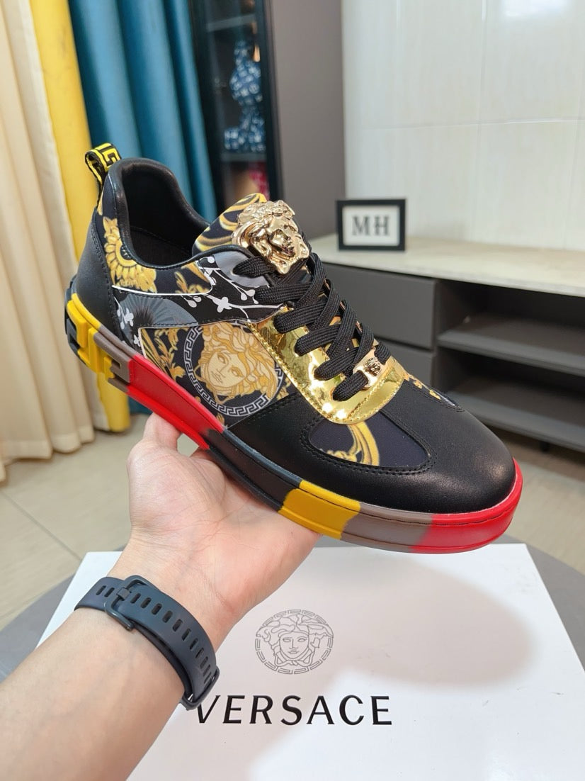 Luxury Versace sneakers held in hand, black with gold prints, red and yellow sole trim