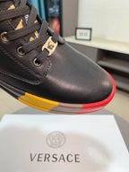 Close-up of black sneaker quarter panel with lace loops and gold buckle charm; red/yellow sole