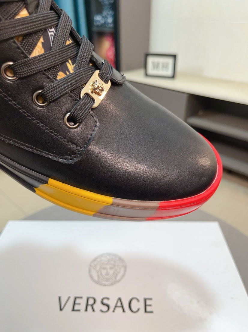 Close-up of black sneaker quarter panel with lace loops and gold buckle charm; red/yellow sole