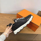 Black unisex sneaker held in hand, white laces and chunky white sole.
