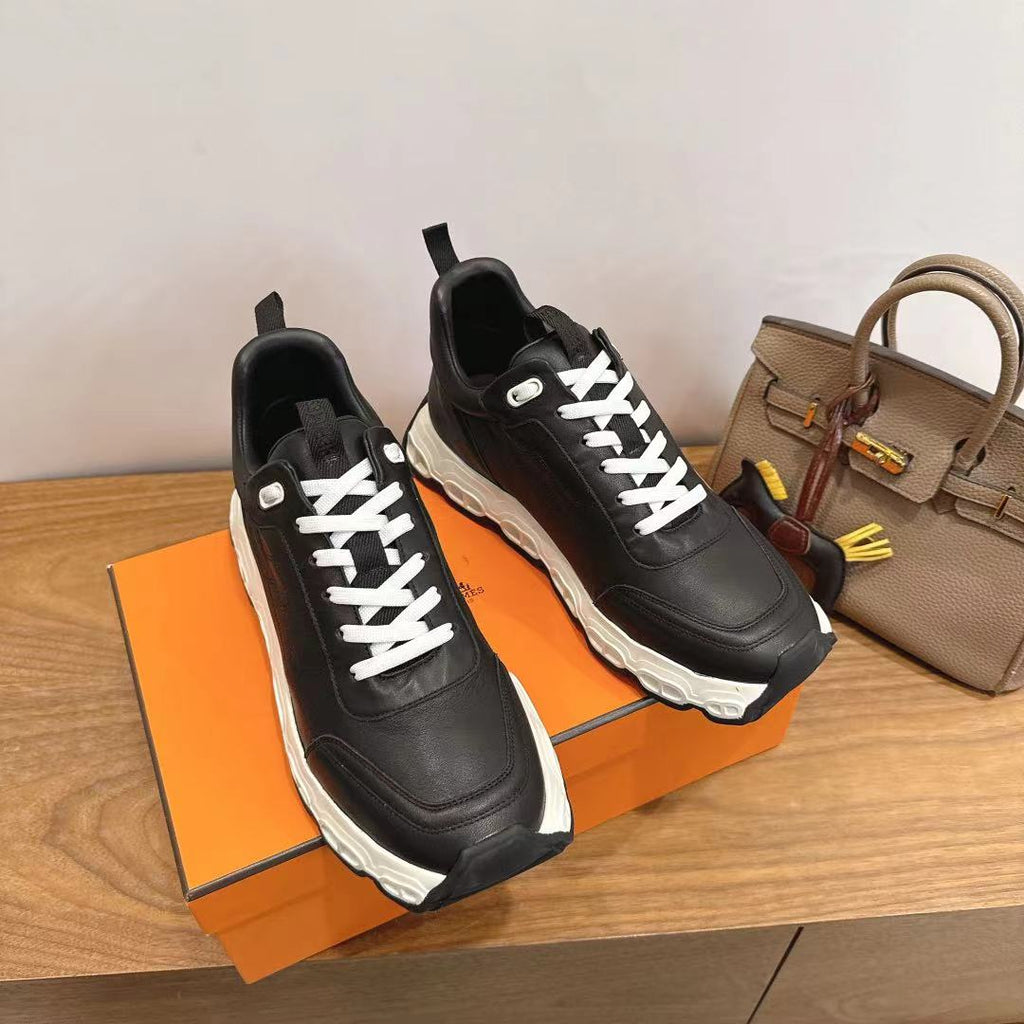 Black unisex sneakers with white laces on orange box, chunky white soles.