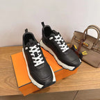 Black unisex sneakers with white laces on orange box, chunky white soles.