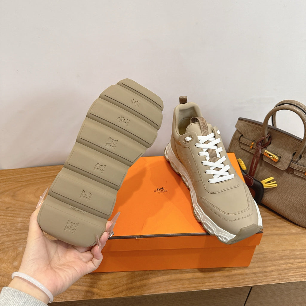Beige lace-up sneakers with white treaded sole bottoms, shown on box lid.
