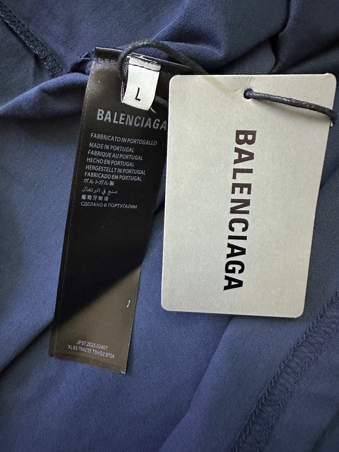 Balenciaga garment tags and size label attached to dark blue T-shirt fabric