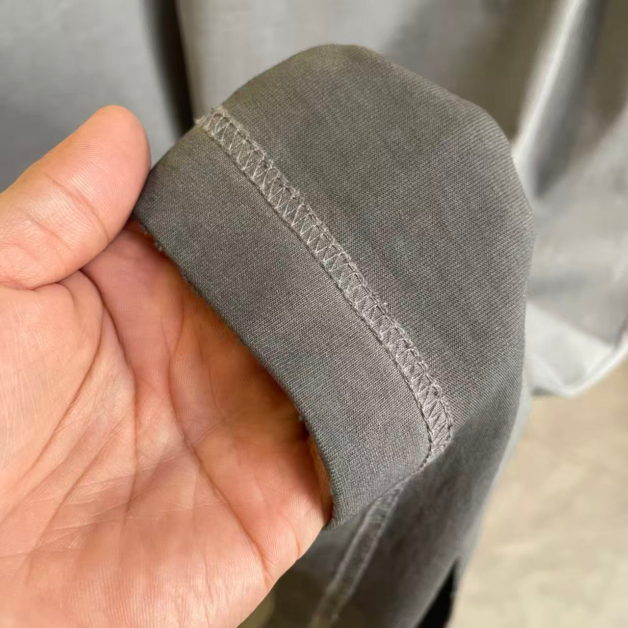 Gray T-shirt hem cuff with stitched edge, held in hand