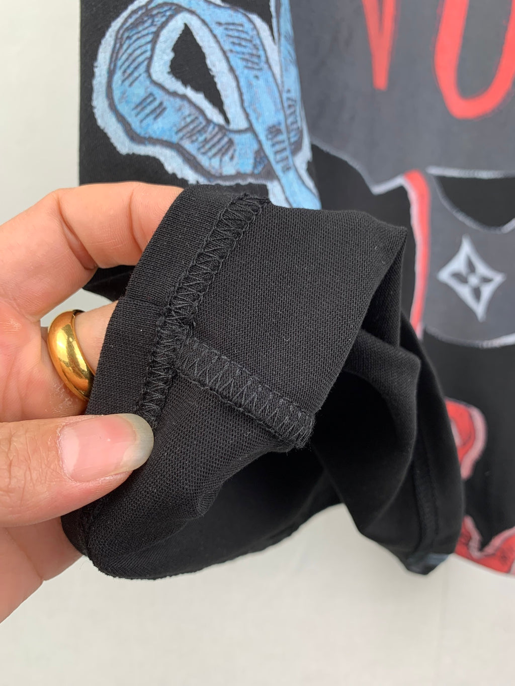 Louis Vuitton black T-shirt cuff detail with stitched fold and graphic print behind