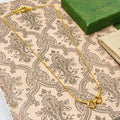 Gold-tone necklace chain with heart-shaped clasp, laid on patterned fabric