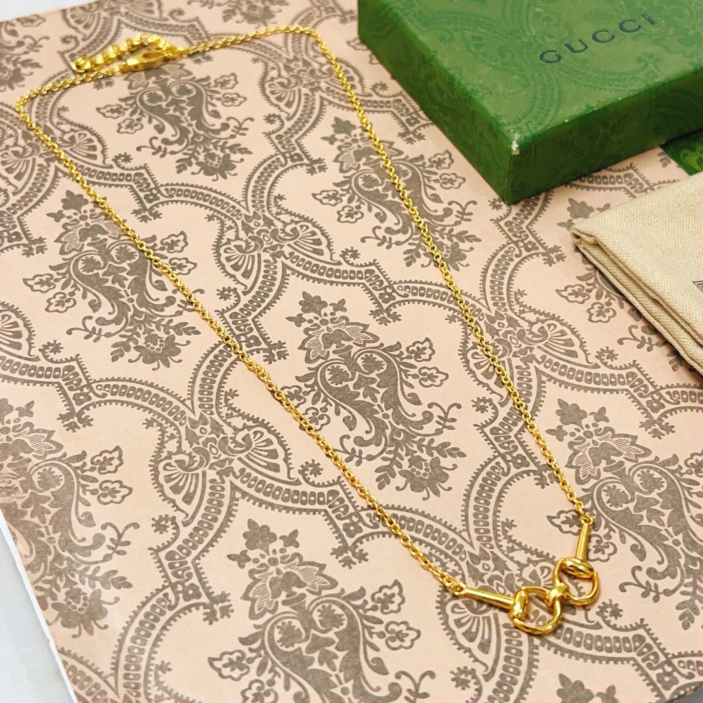 Gold-tone necklace chain with heart-shaped clasp, laid on patterned fabric