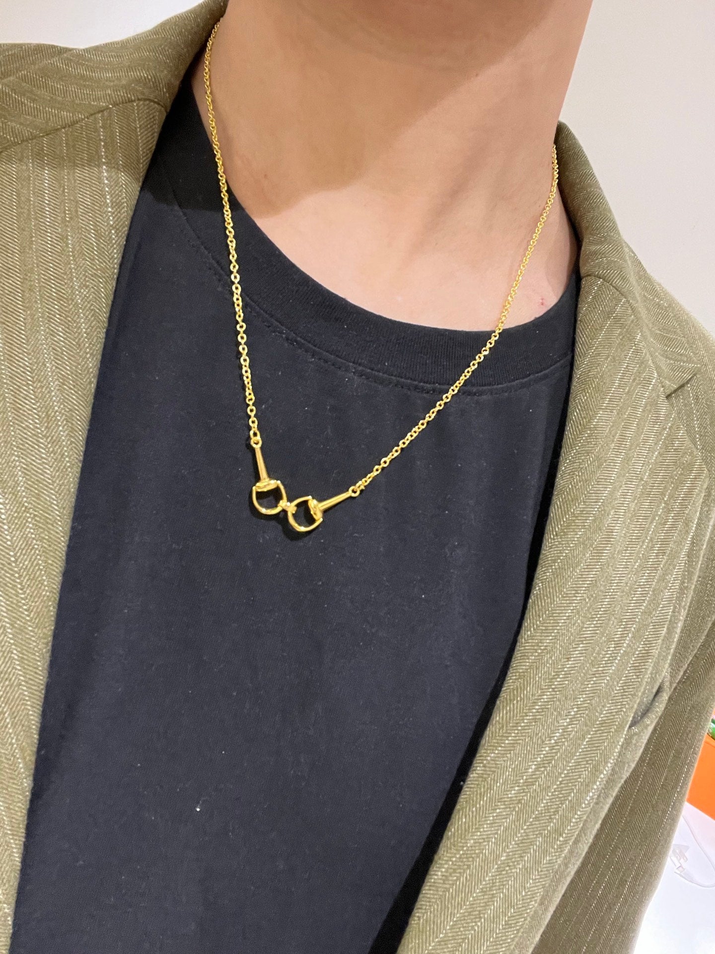 Gold-tone necklace with heart-shaped clasp worn on the neckline of a dark top