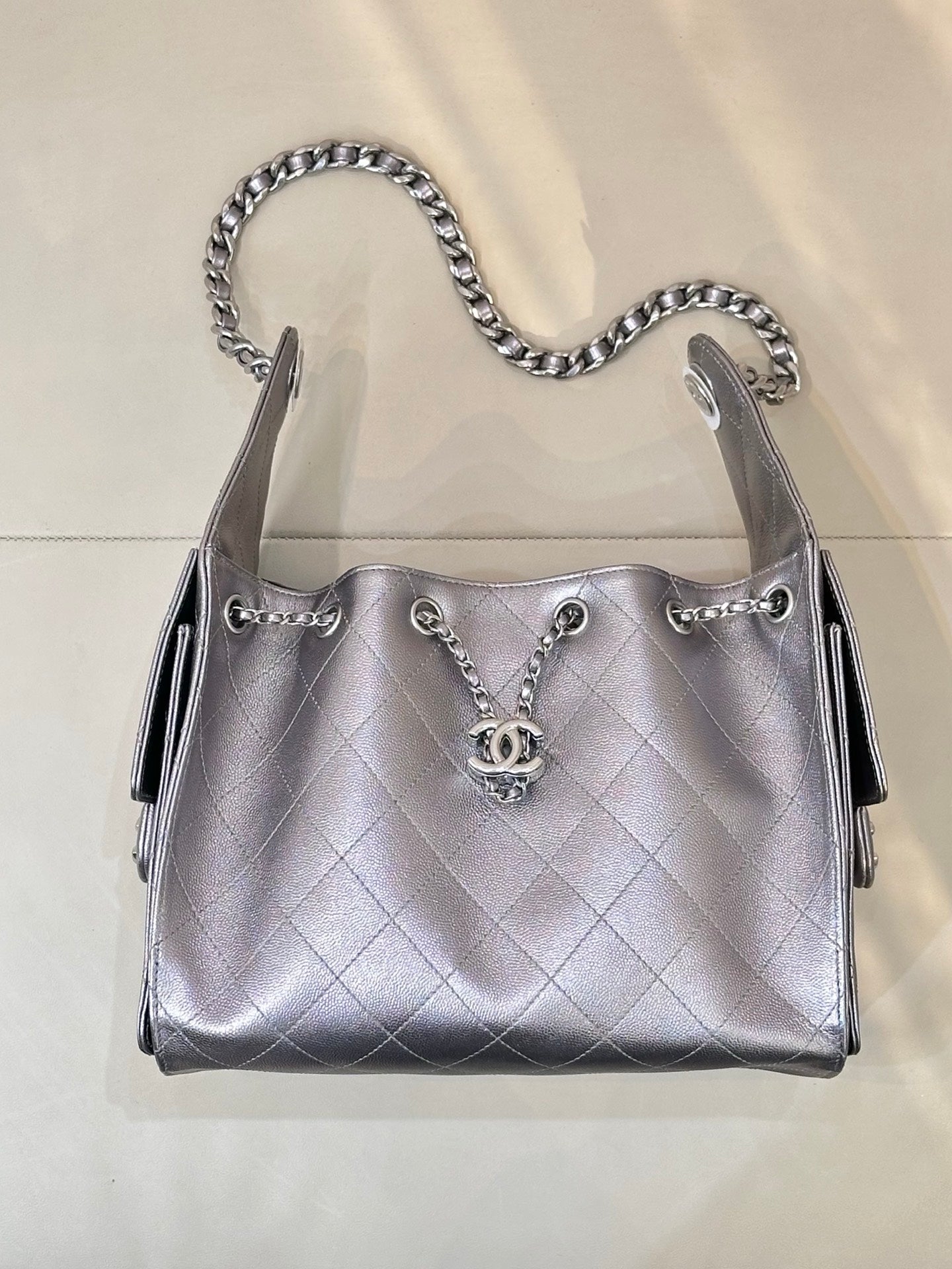 Quilted leather shoulder bag with chain handles, front Chanel CC charm, and side tabs, silver