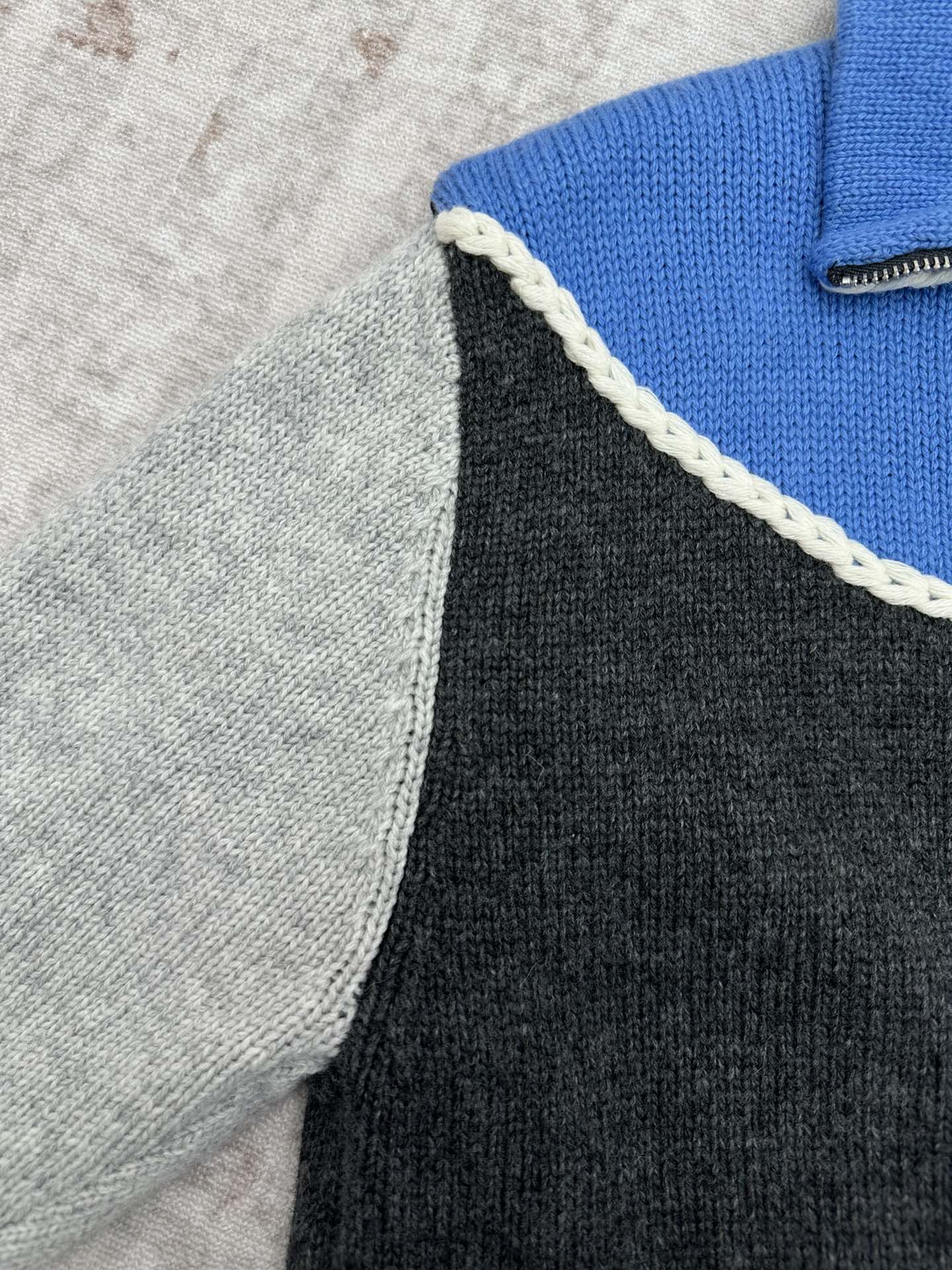 Shoulder seam detail on a knit vest with white braided trim separating blue and dark gray