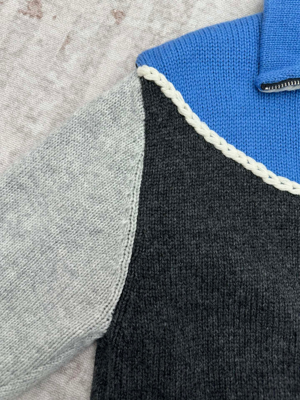 Knit sweater side panel close-up with white braided trim along the zipper edge