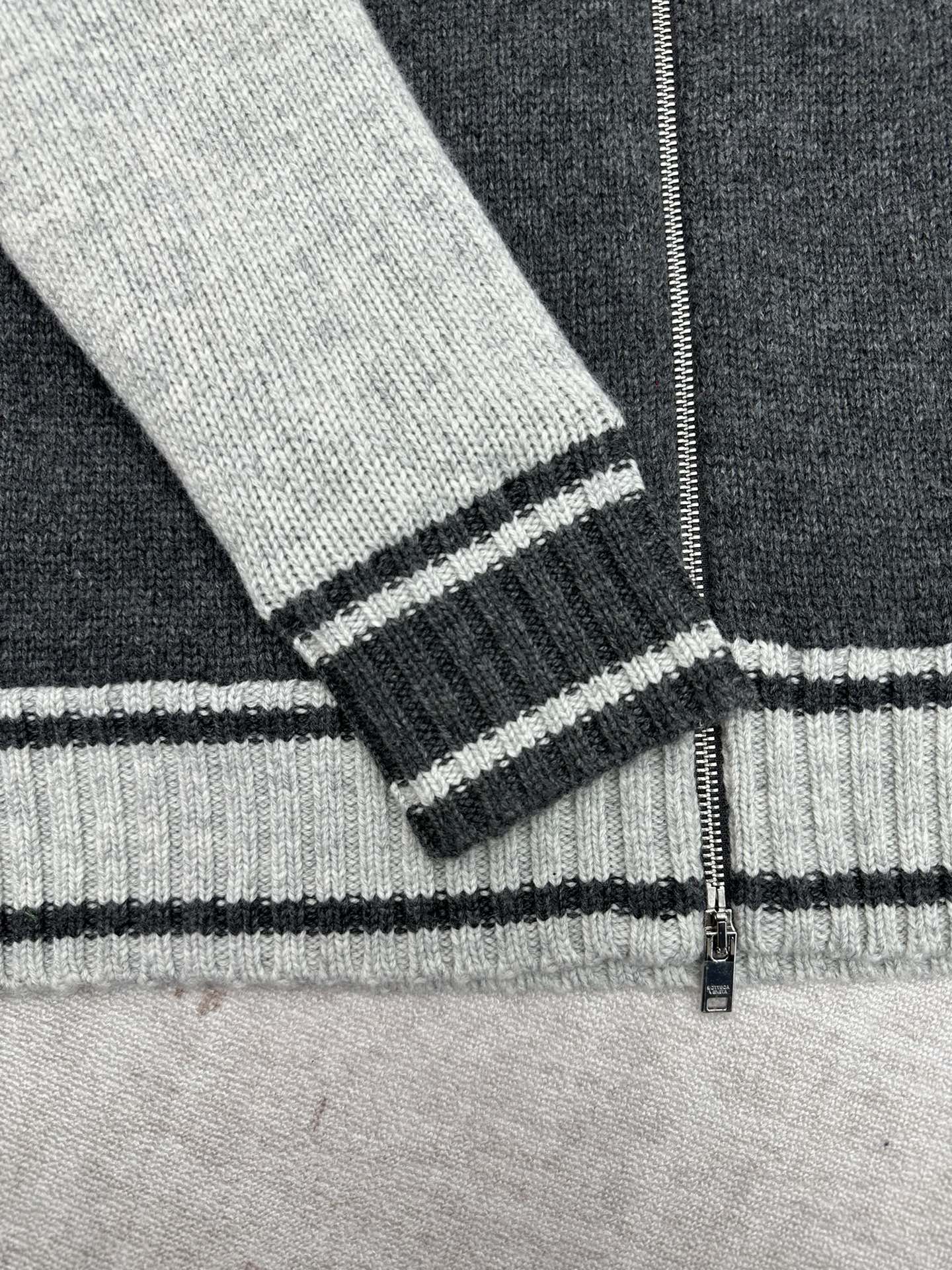 Ribbed sweater cuff with white and black stripes near the zipper opening
