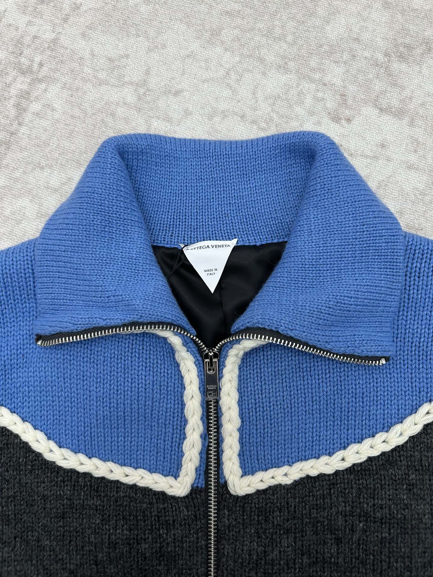 Knit vest neckline detail with blue collar, black lining, and zip with white trim