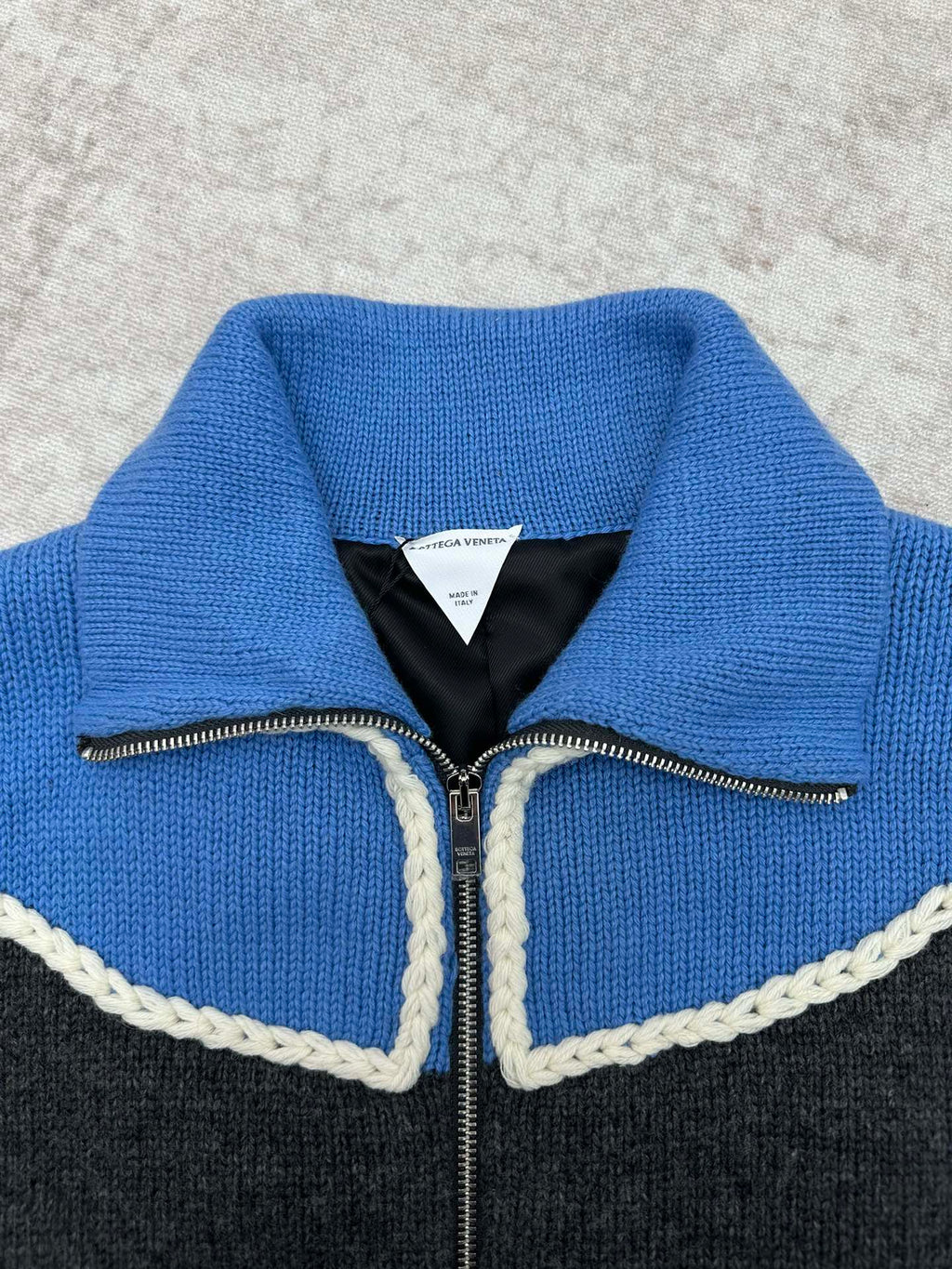 Knit zip sweater neckline close-up with blue knit, black lining, and white trim