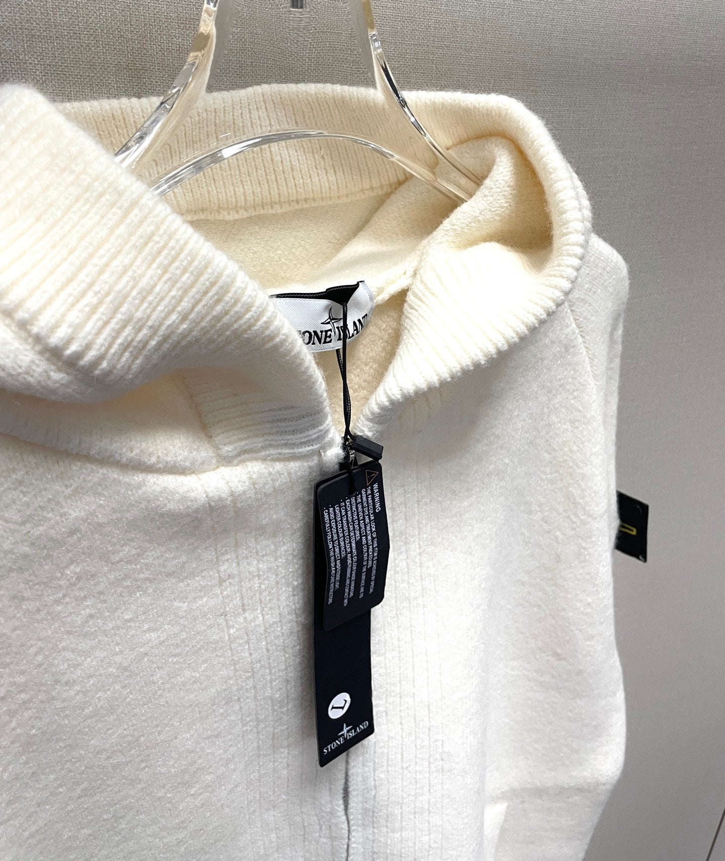 White zip-up hoodie hood close-up with hanging Stone Island product tag
