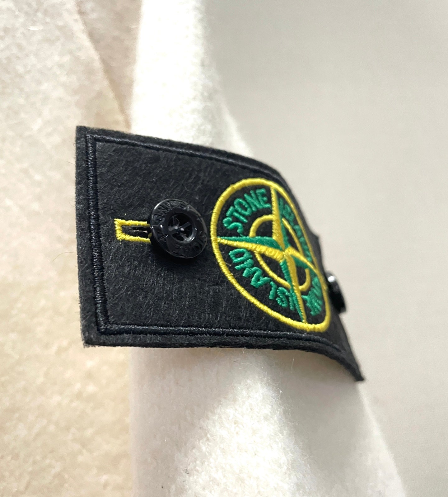 White hoodie sleeve dark patch with circular yellow Stone Island logo emblem
