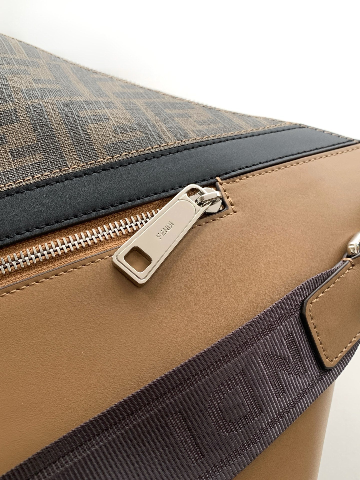 Close-up of tan leather panel and zip track on dark monogram bag
