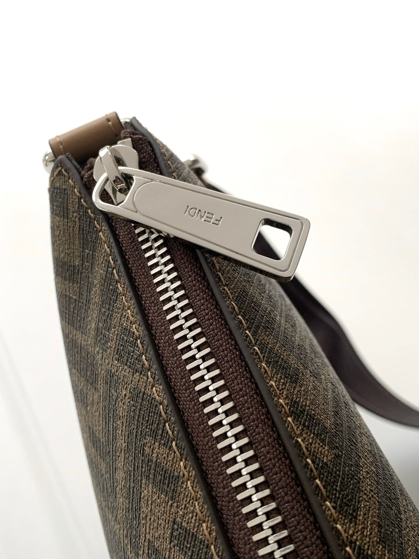 Close-up of monogram zip pocket with metal pull on textured dark canvas