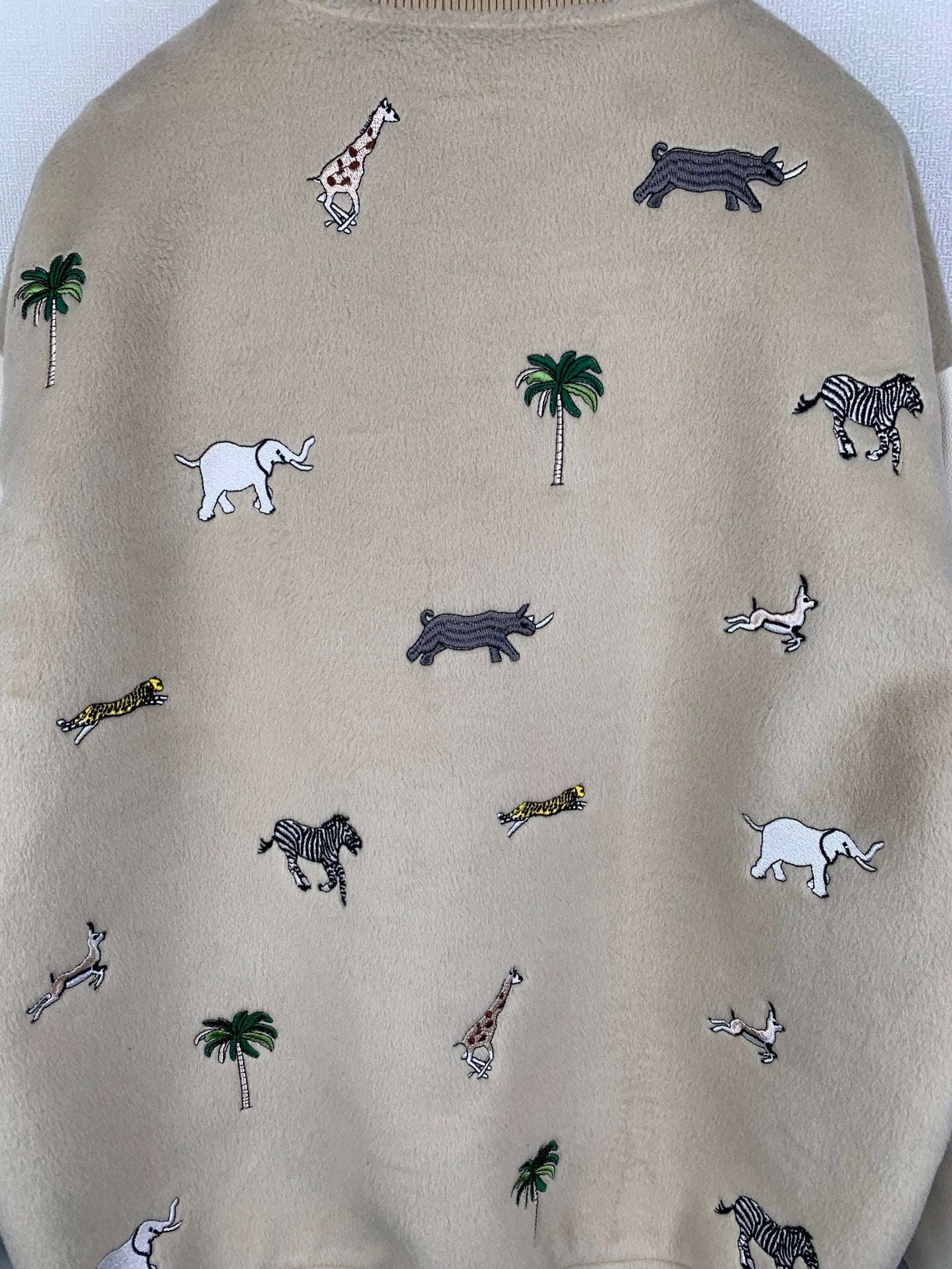 Beige sweatshirt with scattered embroidered animals and palm trees