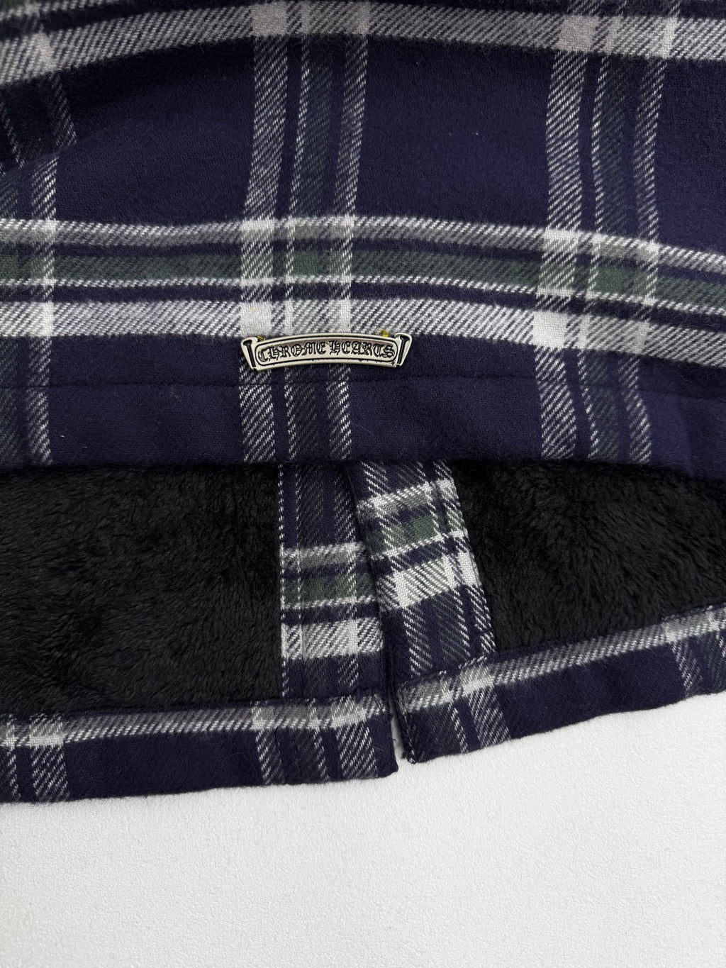 Long dark plaid jacket with front zipper and metal brand badge at collar