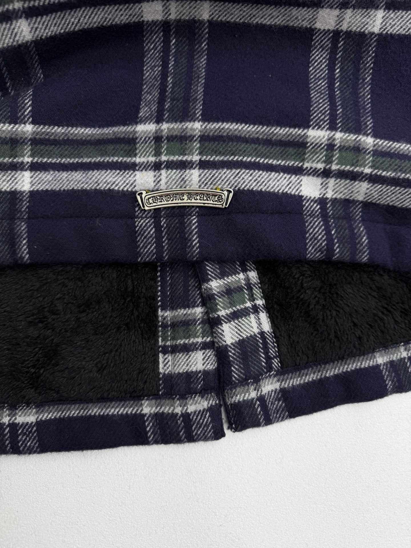 Long dark plaid jacket with front zipper and metal brand badge at collar