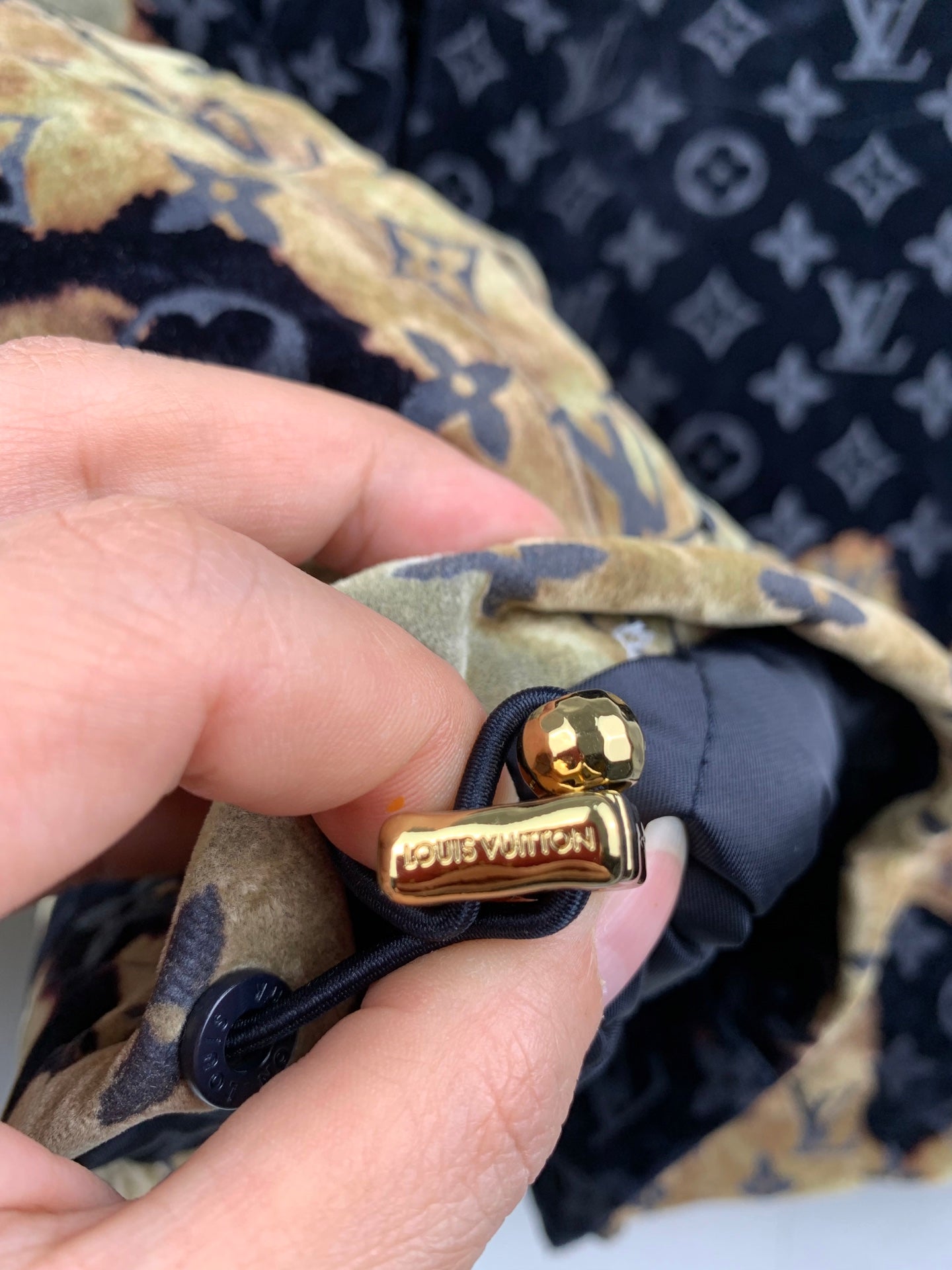 Louis Vuitton long jacket fastener detail, dark strap with gold button and emblem