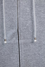 Light gray hoodie showing center zipper and drawstring ends with small beads.