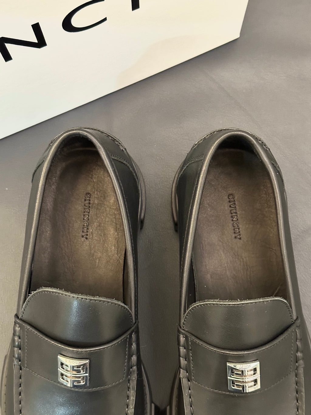 Close-up of dark leather loafer uppers with square logo buckle and stitched trim