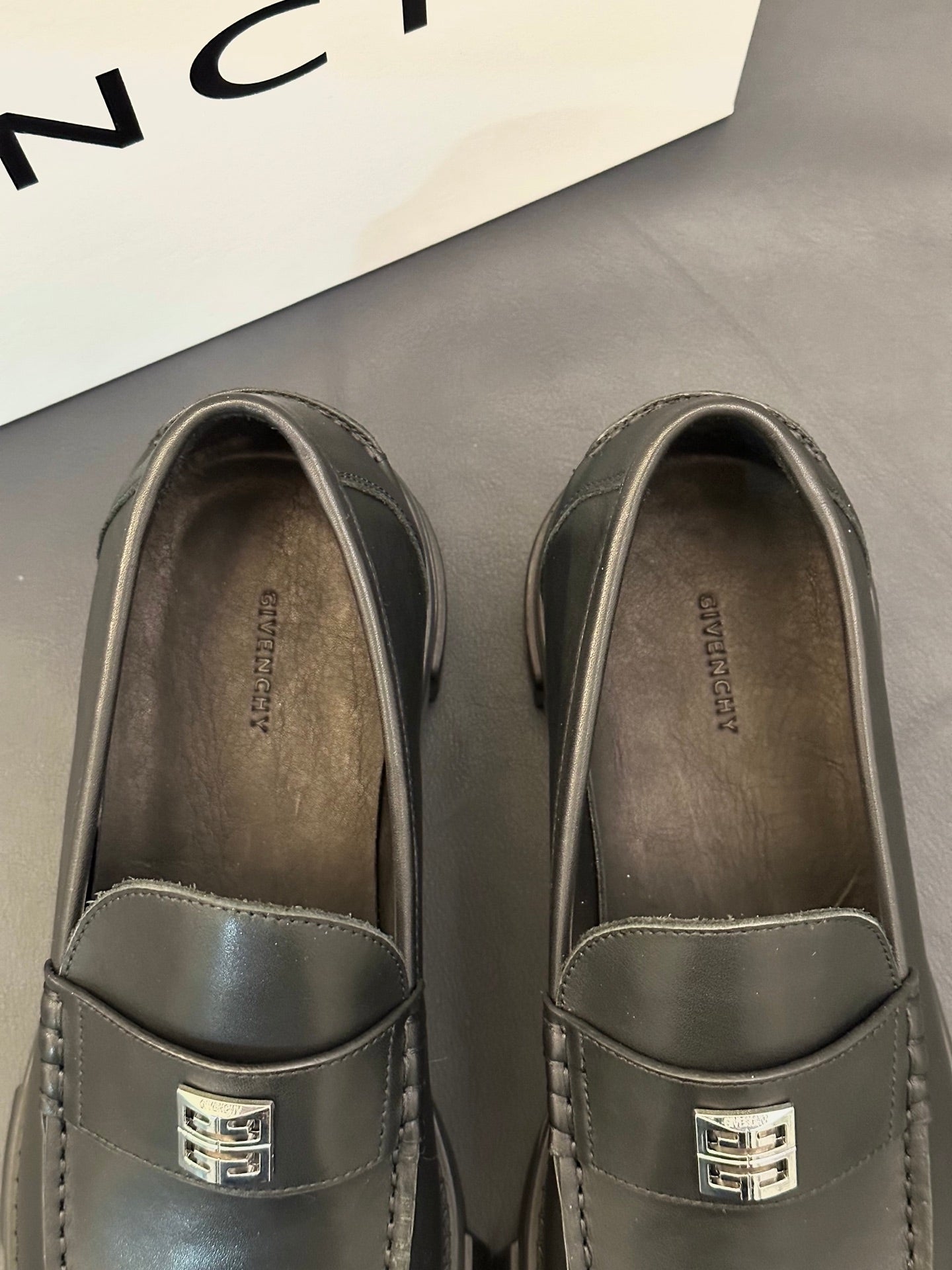 Close-up of dark leather loafer uppers with square logo buckle and stitched trim