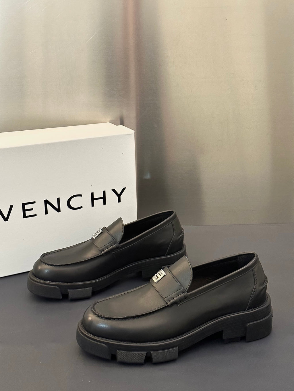 Dark leather loafer pair with square logo buckle strap and chunky rubber outsole