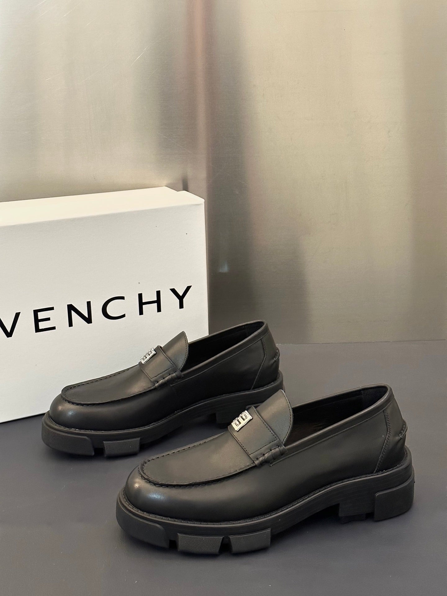 Dark leather loafer pair with square logo buckle strap and chunky rubber outsole