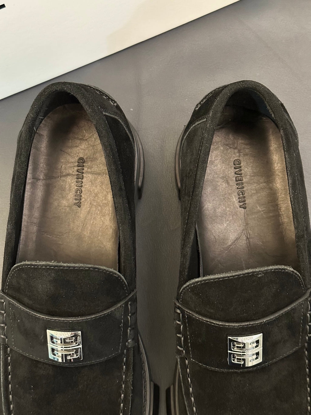 Black suede loafers close-up: front logo strap and stitched seam, interior lining visible