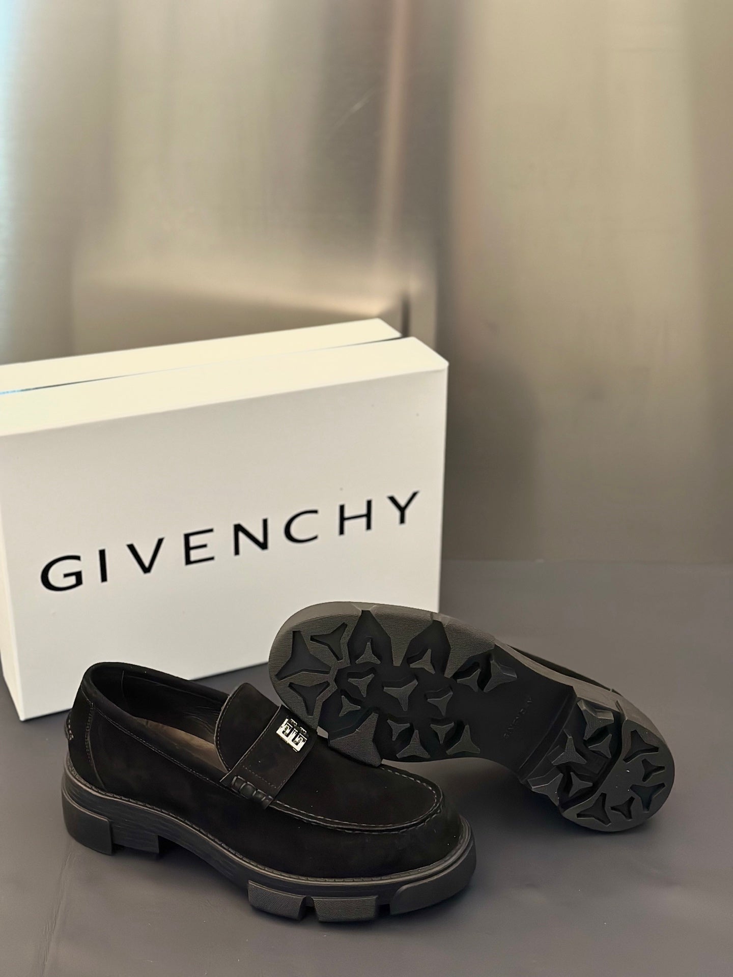 Black suede loafers with square logo strap; open outsole with tread pattern