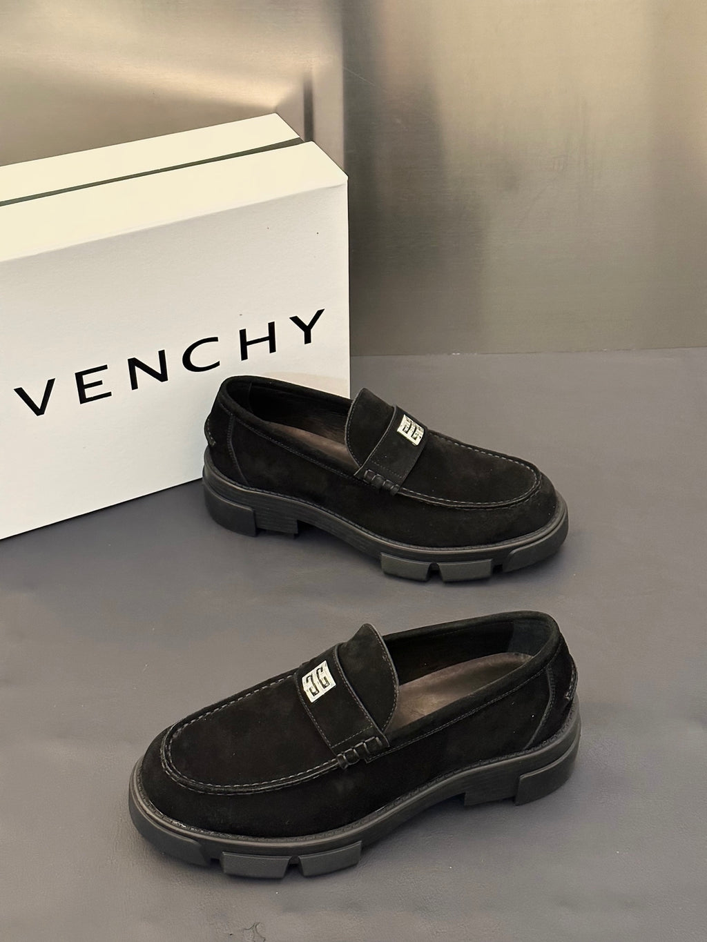 Black slip-on loafers with logo strap detail and rugged tread sole, angled pair