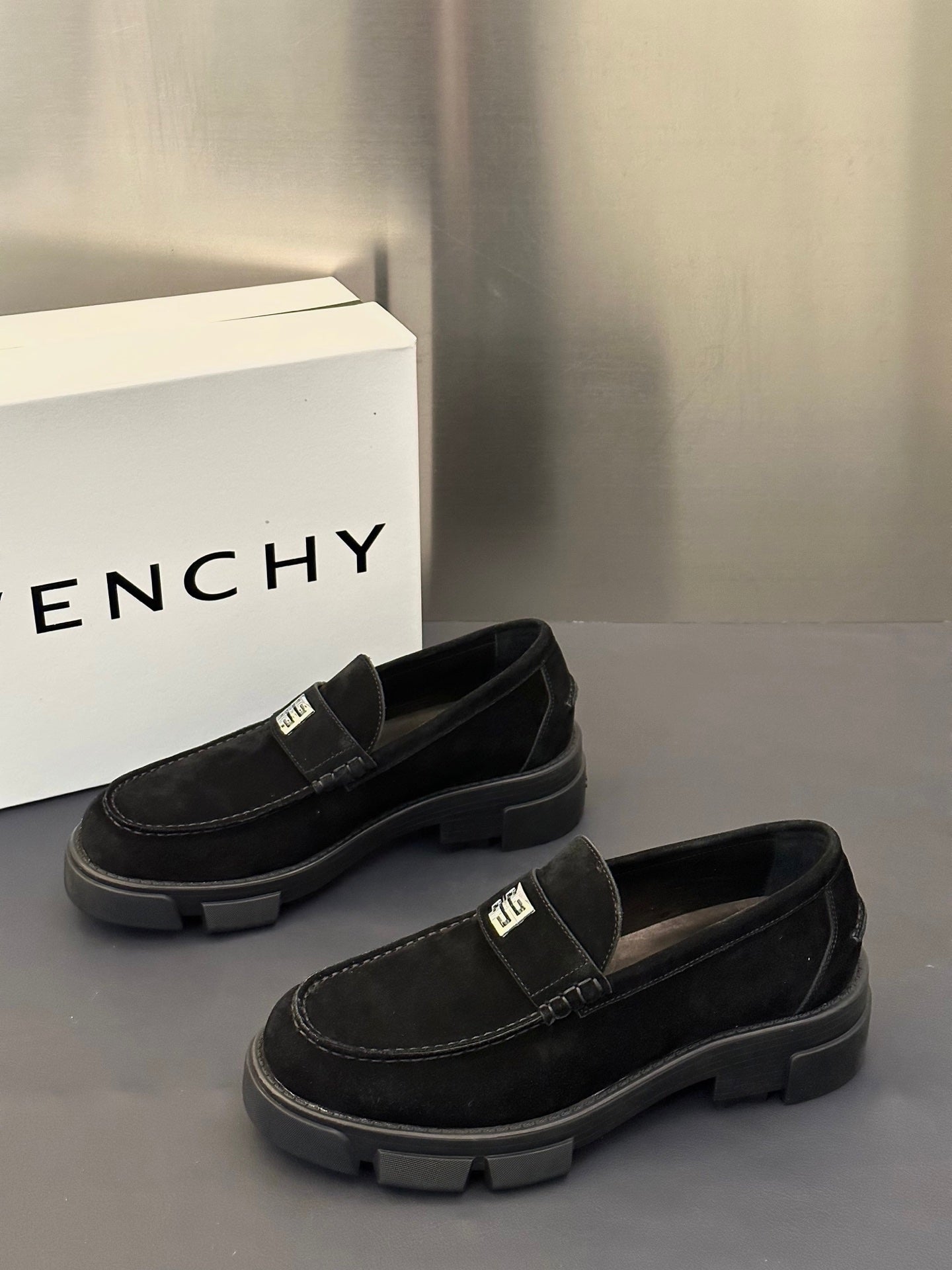 Black suede loafers with logo strap and thick tread sole, front three-quarter view