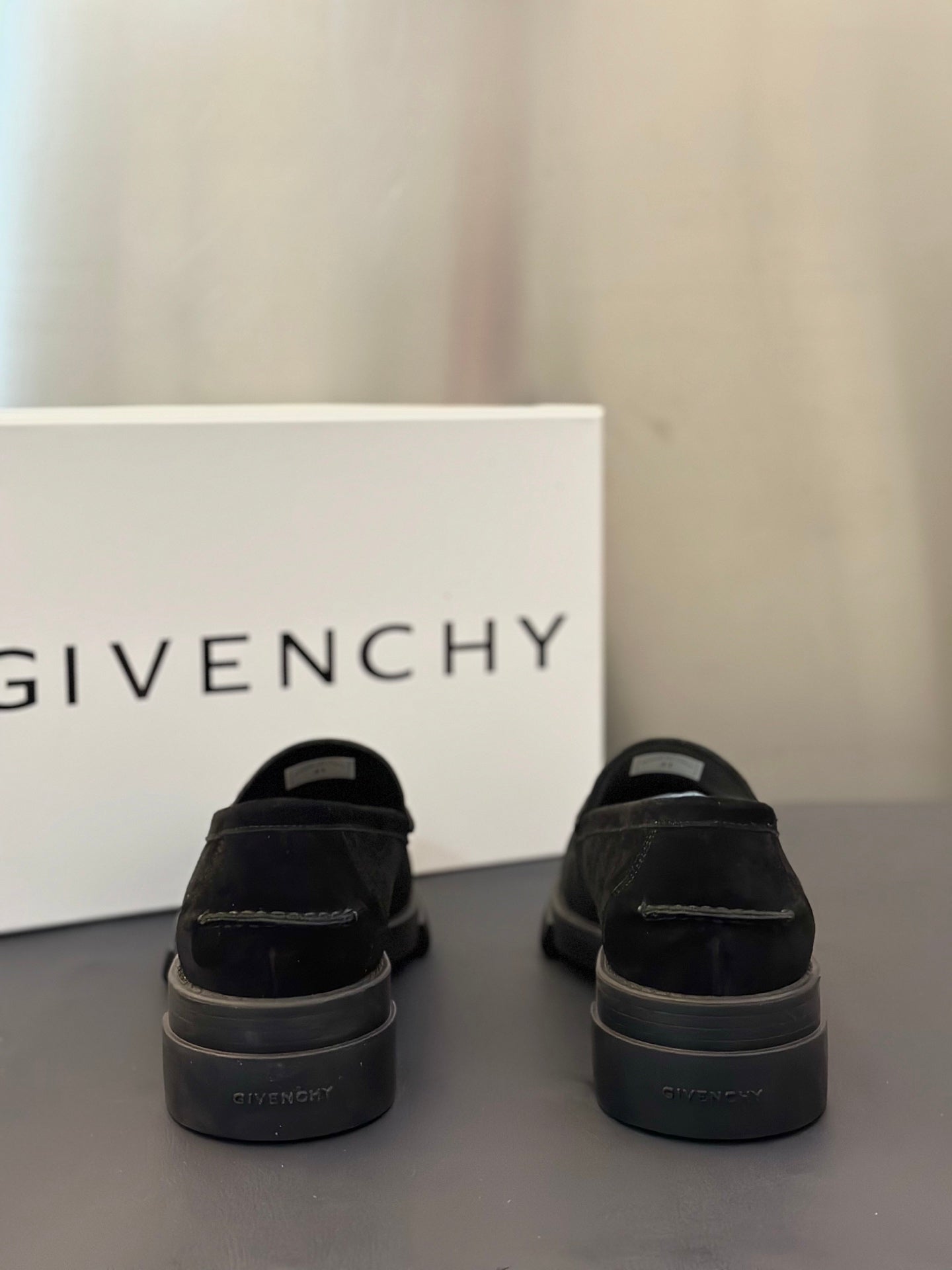 Black loafers from heel view with rear branding and chunky sole, pair on surface