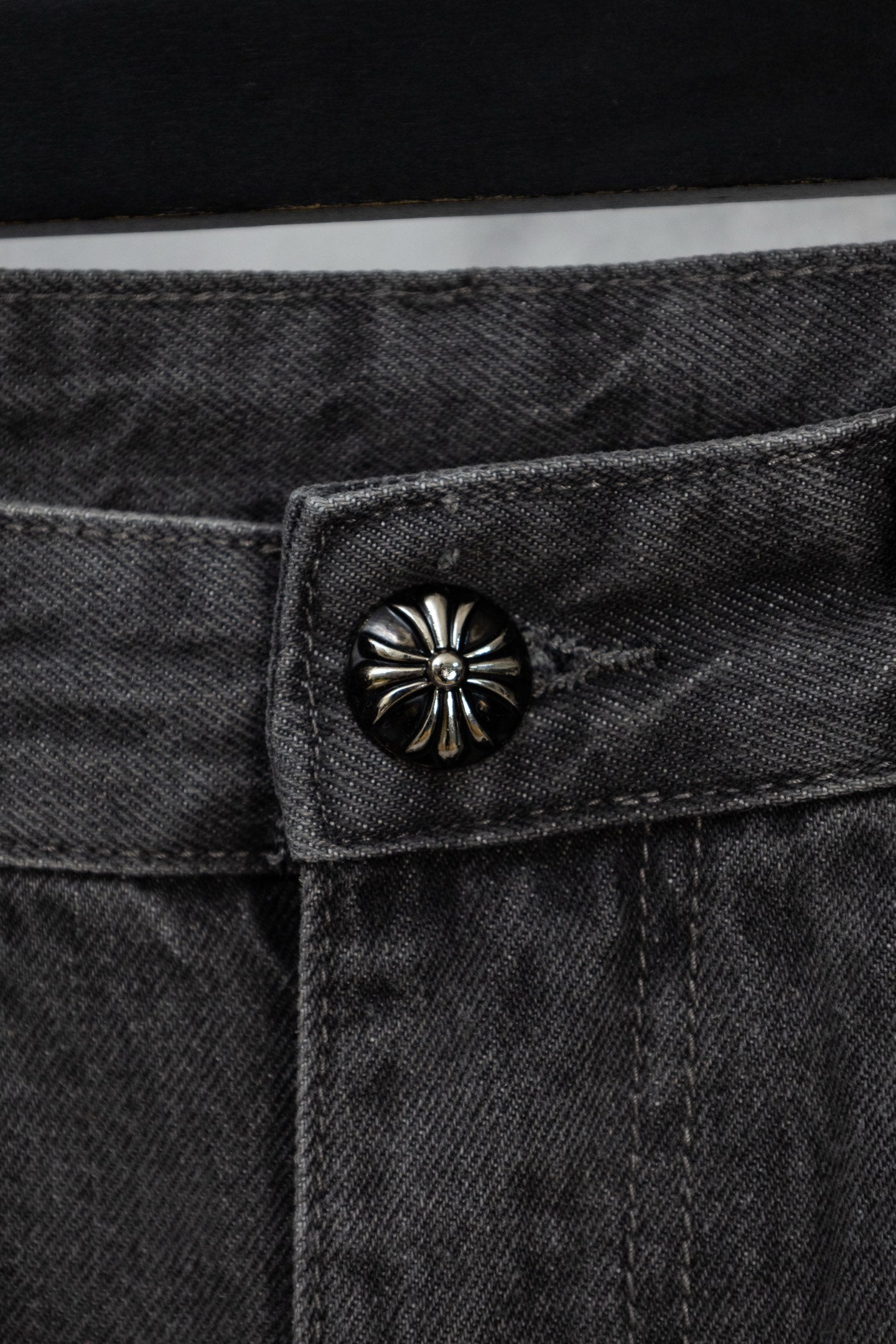 Dark denim pants with round metal button at the waistband