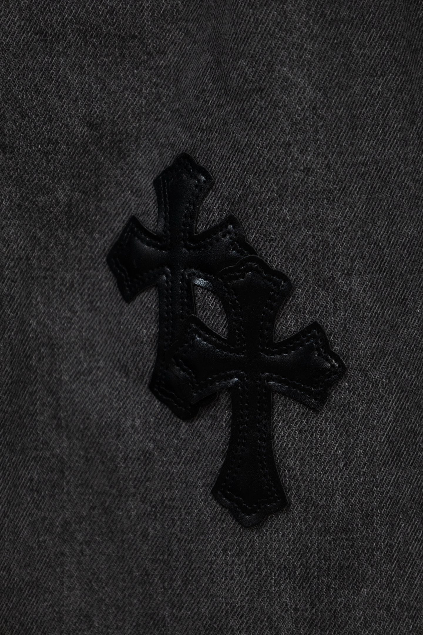 Black cross appliqué detail on dark gray denim