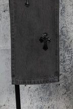 Dark gray denim pants hem with black cross appliqué near the cuff