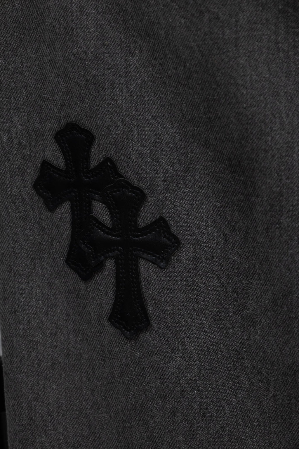Black cross appliqué on dark gray denim pant leg