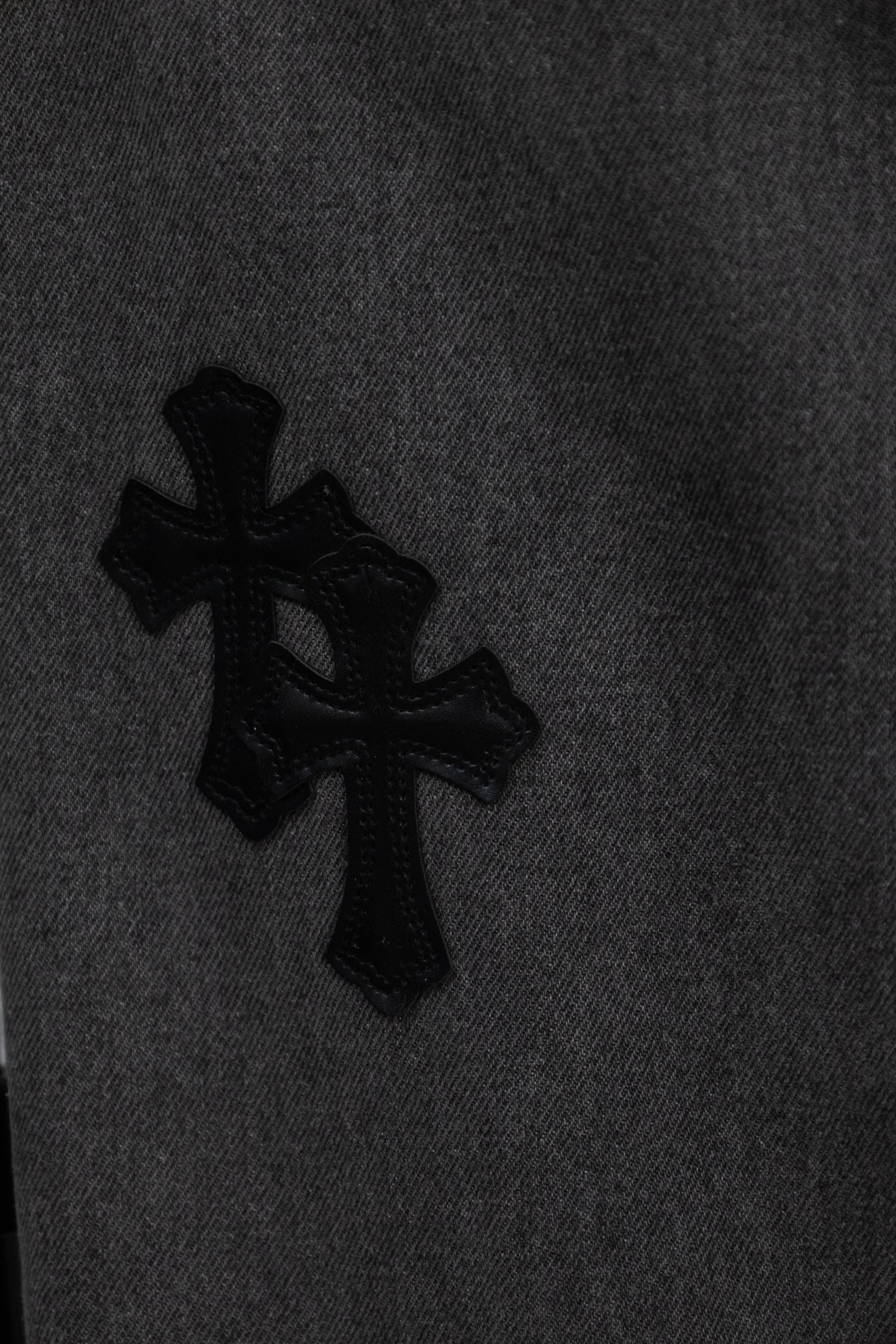 Black cross appliqué on dark gray denim pant leg