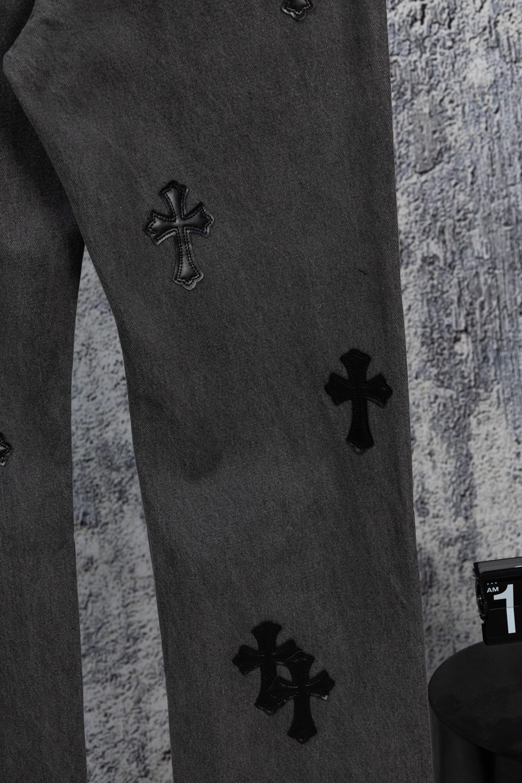 Dark gray denim pants leg with small black cross appliques at staggered spots