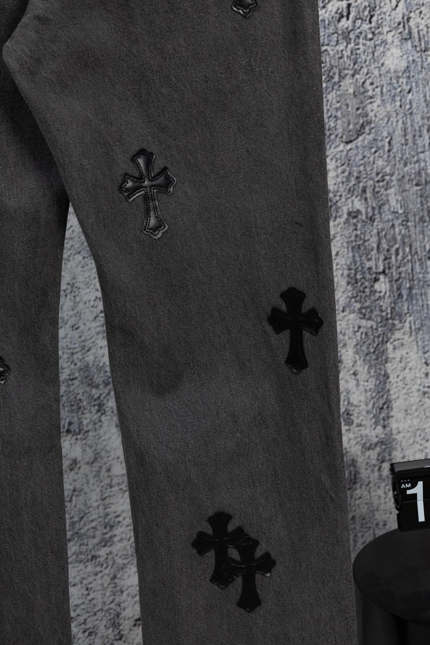 Dark gray denim pants leg with small black cross appliques at staggered spots